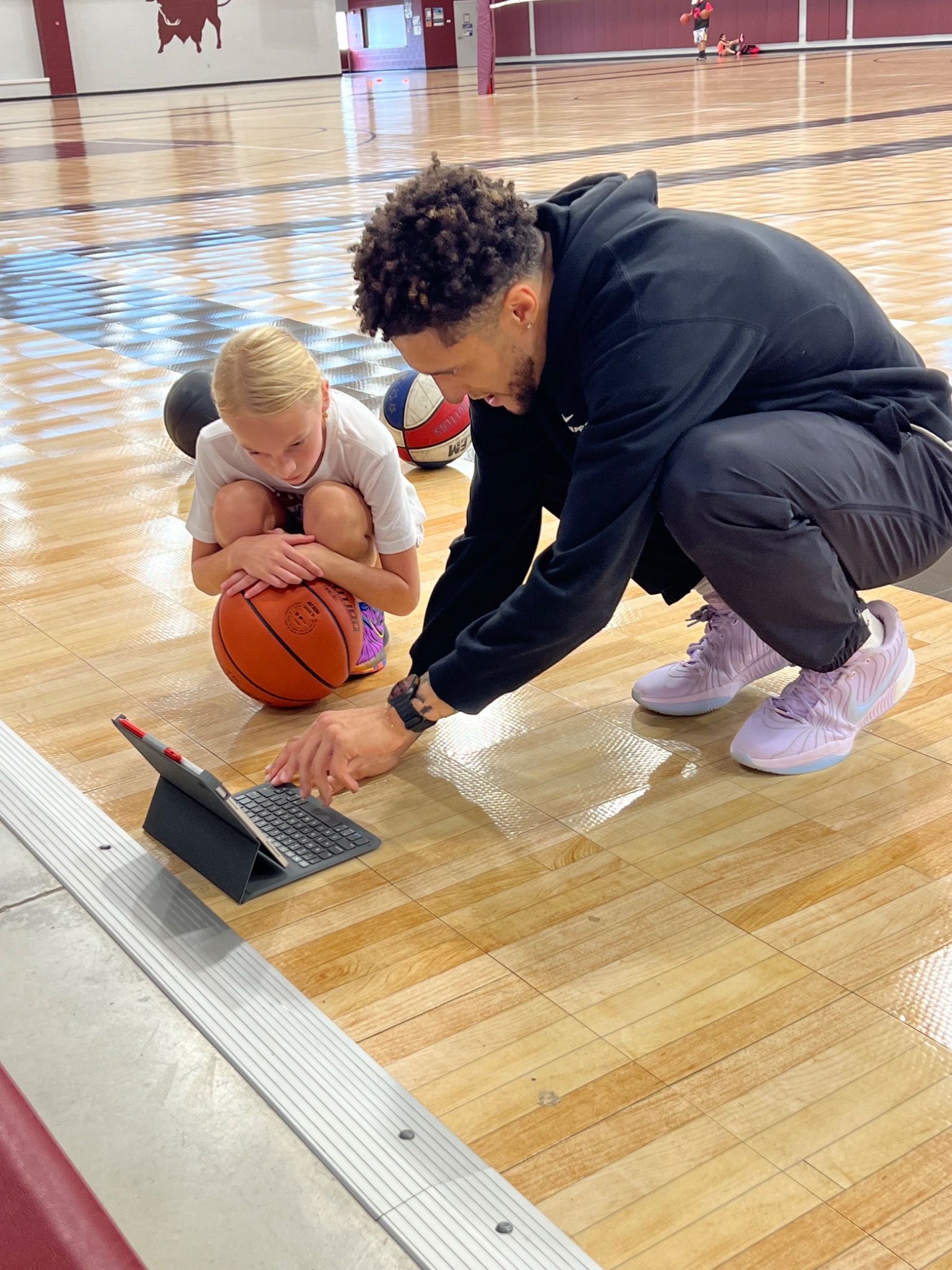 Coach Sam Baker reviewing basketball film with a young athlete during a gym training session